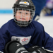 A young boy, in a black Bauer helmet and a navy USA Hockey/NHL jersey sits on the ice and smiles during Try Hockey For Free Day