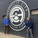 Two men stand next to the Asheville City Soccer club crest.
