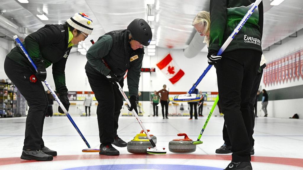 Curler with helmet sweeps a stone
