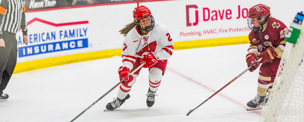 Wisconsin Sophomore Kirsten Simms, in her white and red Wisconsin jersey, skates around the ice with the puck.